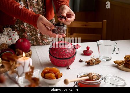 Gemütliche Herbsttage. Frau in orangefarbenem Pullover braut Tee in roter Teekane auf dem Tisch mit Leinentischdecke. Aromatische Stimmung. Herbststimmung. Tee trinken.als Stockfoto