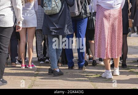 Eine große Gruppe von Menschen in verschiedenen Kleidern steht auf einer Stadtstraße mit dem Rücken zur Kamera Stockfoto