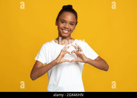 Happy teen afroamerikanische Mädchen Schüler Blogger in weißem T-Shirt zeigen Herzgeste mit Händen Stockfoto