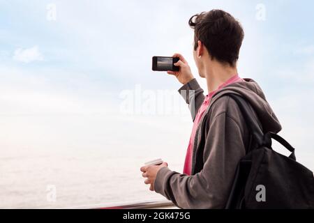 Rückansicht eines jungen Mannes mit Rucksack, der ein Foto mit einem Mobiltelefon macht, Konzept der Technologie und des tausendjährigen Lebensstils, Platz für Text kopieren Stockfoto