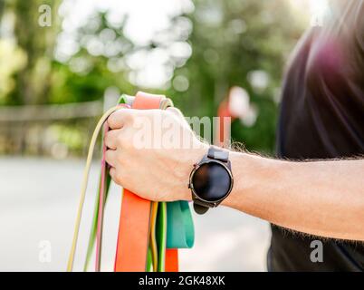 Starker Mann, der in der Hand hält und einen Fitness-Tracker mit bunten Gummibändern im Stadion im Freien trägt. Athlet männlich Person während wo Stockfoto