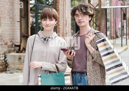 Porträt eines jungen Paares mit Einkaufstaschen, das beim gemeinsamen Einkaufen in der Stadt die Kamera anschaut Stockfoto