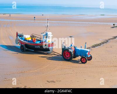 Crab oder Hummer, Fischer, die einen Traktor fahren, der ihr Boot SH278, Isis, aus dem Meer schleppt Redcar Cleveland UK Stockfoto