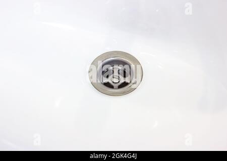 Metallisches Wasserabflussloch im weißen Keramikwaschbecken im Badezimmer in der Nähe. Stockfoto