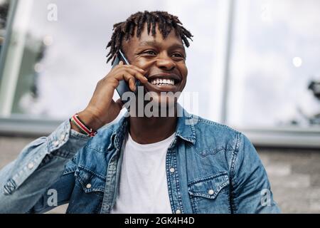 Afroamerikanischer Mann, der vor dem Hintergrund eines Glasgebäudes telefoniert, afrikanischer Geschäftsmann mit Mobiltelefon Stockfoto