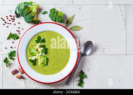 Brokkoli-Suppenpüree mit Feta-Käse in Teller auf grauem Fliesenhintergrund mit Zutaten, Draufsicht. Kochen gesundes Essen Konzept. Stockfoto