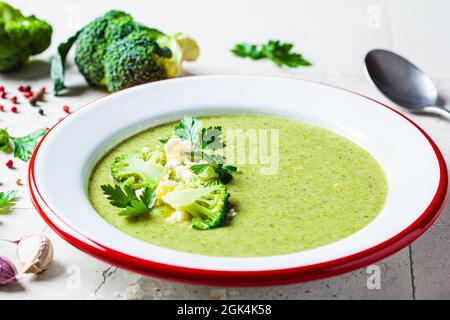 Brokkoli-Suppenpüree mit Feta-Käse in Teller auf grauem Fliesenhintergrund mit Zutaten. Kochen gesundes Essen Konzept. Stockfoto