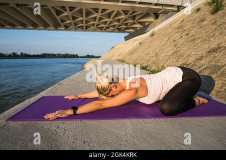 Junge Frau trainiert im Freien. Sie praktiziert Yoga an sonnigen Tagen. Balasana, Kinderpose. Stockfoto