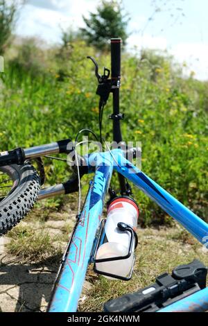GÖTTINGEN, DEUTSCHLAND - 20. Aug 2021: Vertikale Aufnahme eines blauen Mountainbikes, das im Gras liegt und an dem eine Plastikwasserflasche befestigt ist. Außenspor Stockfoto