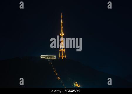 Blick auf den beleuchteten Fernsehturm von Tiflis, der nachts wunderschön auf dem Berg Mtasminda in der Hauptstadt Tiflis in Georgien leuchtet. Stockfoto