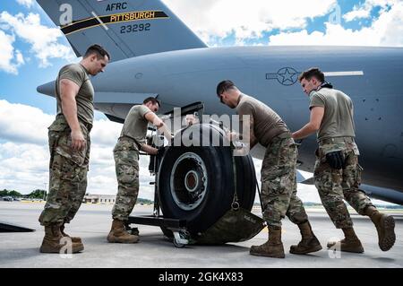 Bei einem Reifenwechsel an der Pittsburgh International Airport Air Reserve Station, Pennsylvania, am 2. August 2021, laden die der 911. Maintenance Group zugeordneten Luftfahrtschipper einen C-17 Globemaster III Reifen auf ein Gurtzeug. Die Piloten verwenden einen speziellen Gurt, um das Gewicht des Rades zu unterstützen, wenn es an den Laschen des Flugzeugs ausgerichtet wird. Stockfoto