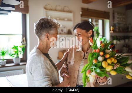 Erwachsene Tochter besucht glückliche ältere Mutter zuhause, Muttertag oder Geburtstagsfeier. Stockfoto