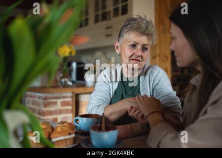Traurige ältere Mutter, die zu Hause mit der erwachsenen Tochter Tee trinkt und spricht. Stockfoto