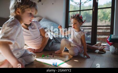 Nicht erkennbarer Vater mit zwei kleinen Kindern, die zuhause ausruhen und Brettspiel spielen. Stockfoto