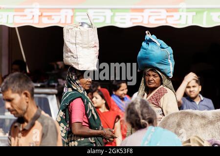 Orchha, Madhya Pradesh, Indien - 2019. März: Zwei indische Frauen mit Taschen auf dem Kopf stehen auf einem überfüllten Marktplatz in der Stadt Orchha. Stockfoto