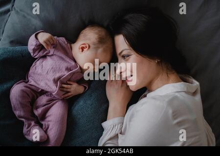 Draufsicht auf eine glückliche junge Mutter mit ihrem neugeborenen Mädchen, das zuhause auf dem Sofa liegt. Stockfoto