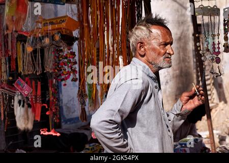 Orchha, Madhya Pradesh, Indien - 2019. März: Ein älterer indischer Mann, der vor einem Geschäft steht und eine bidi-Zigarette raucht. Stockfoto