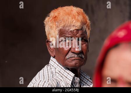 Orchha, Madhya Pradesh, Indien - März 2019: Ehrliches Porträt eines älteren indischen Mannes mit orange gefärbtem Haar, der intensiv und nachdenklich starrt. Stockfoto