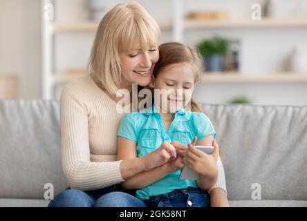 Glückliche reife Frau und Enkelin mit Handy Stockfoto