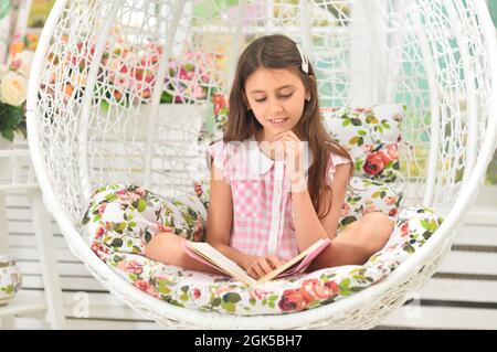 Glückliches kleines Mädchen, das Buch auf Schaukel liest Stockfoto