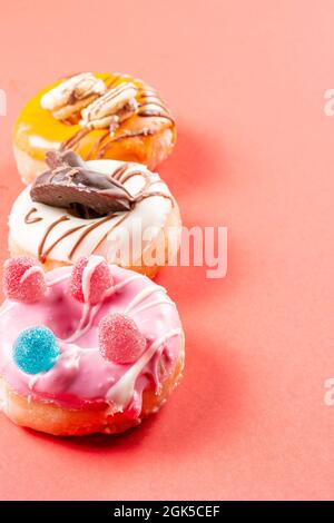 Foto von 3 Donuts, die mit Keksen und Jelly Beans dekoriert sind.die Donuts sind in Erdbeerschokolade, dunkle Schokolade und weiße Schokolade getaucht.Foto aufgenommen Stockfoto