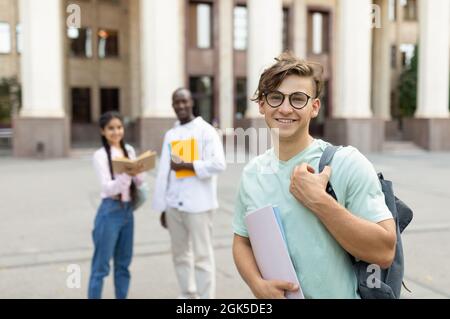 Student Kerl im Freien auf dem Campus mit seinen Klassenkameraden und Universitätsgebäude auf dem Hintergrund Stockfoto