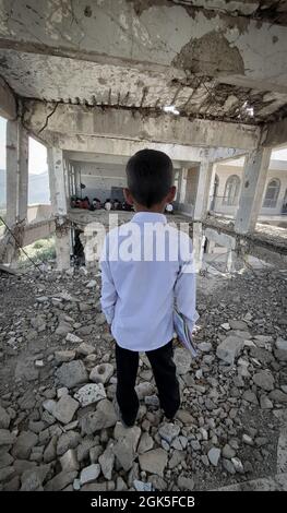 Taiz Jemen - 07. Okt 2020 : Ein jemenitisches Kind in einer vom Krieg zerstörten Schule schaut Klassenkameraden an, die drinnen studieren Stockfoto