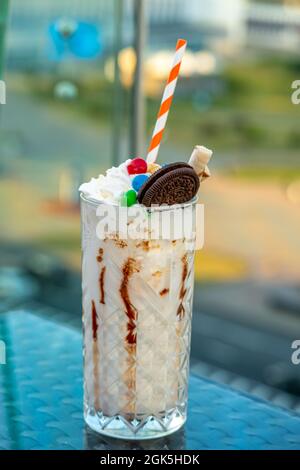 Milchshake in einem Glas mit bunten Süßigkeiten, Keksen und Schokolade steht auf dem Tisch Stockfoto