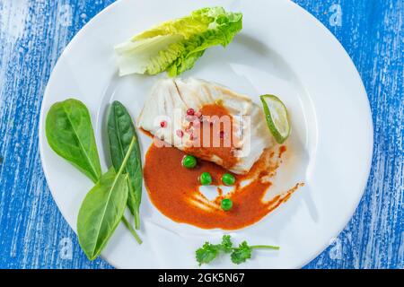 Gedünstetes Kabeljaufilet mit Paprikasoße und Salatblättern. Stockfoto