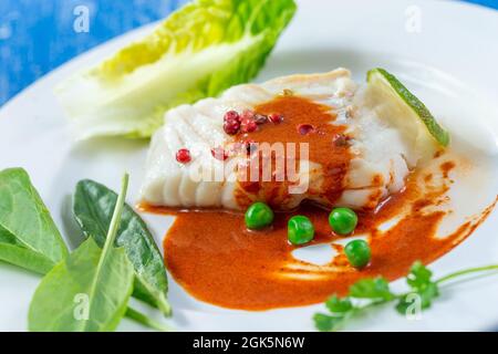 Gedünstetes Kabeljaufilet mit Paprikasoße und Salatblättern. Stockfoto