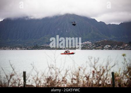 US-Militärpersonal mit dem Marine Corps Base Hawaii Provost Marshal’s Office und Waterfront Operations post Security on a marine vessel, während ein CH-53 Super Hengst, der an Marine Heavy Helicopter Squadron 463 befestigt ist, während Lethal Breeze 2021, MCBH, 10. August 2021, über Bord fliegt. Lethal Breeze ist eine Übung, die die Fähigkeit der Basis zeigt, während eines dynamischen Vorfalls effektiv zu reagieren, zu kommunizieren und Operationen über mehrere Standorte hinweg zu koordinieren. Stockfoto