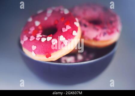 Schöne leckere rosa Donuts mit Streuseln in Form von Herzen und mit Erdbeerfüllung sind in einem blauen Teller. Dessert zum Valentinstag. Stockfoto