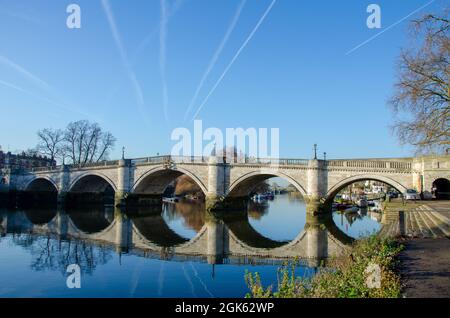 Jet Trails von Flugzeugen, die über die Richmond Bridge nach London Heathrow fliegen, spiegeln sich in der Themse, England Stockfoto