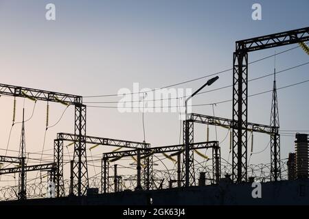 Verteilerstation mit Stromleitungen und Transformatoren. Ein Betonzaun mit Stacheldraht. Stockfoto