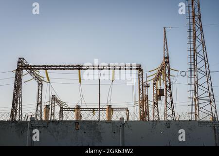 Verteilerstation mit Stromleitungen und Transformatoren. Ein Betonzaun mit Stacheldraht. Stockfoto