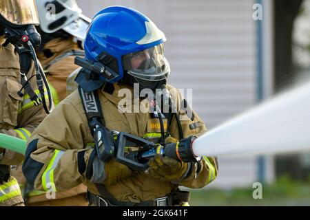 Ein Feuerwehrmann der lettischen Bundeswehr hält einen Schlauch, während er Wasser auf einen simulierten Flugzeugbrand im Alpena Combat Readiness Training Center, Michigan, am 12. August 2021 sprüht. Die Simulation war Teil der Übung Northern Strike 21-2, die die Möglichkeit bietet, Interoperabilität mit anderen Einheiten und multinationalen Partnern aufzubauen, während sie in realistischen Multi-Domain-Umgebungen trainiert. Stockfoto