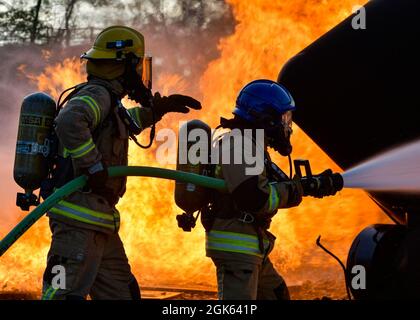 Feuerwehrleute der lettischen Bundeswehr und der estnischen Streitkräfte verwenden einen Löschschlauch, um ein simuliertes Flugzeugfeuer im Alpena Combat Readiness Training Center, Michigan, am 12. August 2021, zu sprühen. Die Simulation war Teil der Übung Northern Strike 21-2, einer von der Nationalgarde gesponserten Übung, bei der 5,100 Teilnehmer aus verschiedenen Staaten und Ländern im National All-Domain Warfighting Center zusammenkamen. Stockfoto
