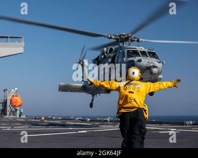 210811-N-LR905-4039 PAZIFISCHER OZEAN (AUG 11, 2021) – der Mate 3rd Class von Aviation Boatswain Nadezhda Zurbriggen leitet einen MH-60S Sea Hawk vom Helicopter Sea Combat Squadron (HSC) 23 an Bord des Expeditionsstützpunktes USS Miguel Keith (ESB 5), 11. August. Die HSC 23 wird an Bord von Miguel Keith an Bord genommen und führt Routineoperationen in der 3. US-Flotte durch. Stockfoto