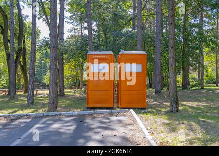 Zwei orangefarbene tragbare Toilettenkabinen im Stadtpark Stockfoto