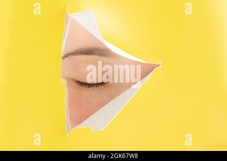 In gelbem Papier mit einem ausgeschnittenen Dreieck in der Mitte, ein menschliches geschlossenes Auge. Stockfoto