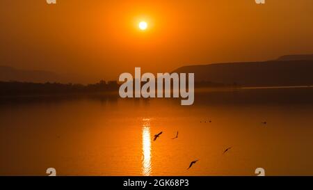 PUNE, INDIEN - 10. Sep 2019: Die wunderschöne Aussicht auf den Sonnenuntergang und die Spiegelung der Sonne im See. Während sich die Vögel dort drüben austun. Stockfoto