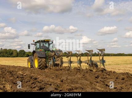 Landwirt in einem Traktor, der im Spätsommer ein Feld pflügt. Stockfoto