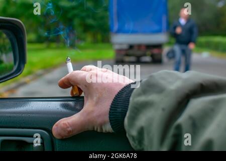 Hand eines Mannes, eines Fahrers, eines Rauchens, das in einem Auto sitzt und eine rauchende Zigarette hält Stockfoto