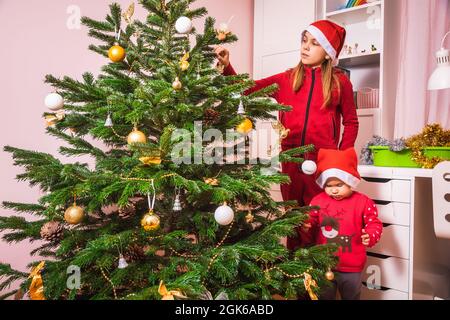 Schwestern in Rot schmücken den Weihnachtsbaum zu Hause Stockfoto