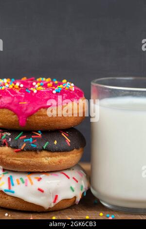 Schönes, süßes Essen. Stapel von glasierten bunten verschiedenen Donuts mit einer Tasse Milch auf einem grauen Hintergrund. Stockfoto