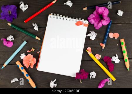 Papier-Notizbuch mit leeren Seiten, zerknitterten Papierkugeln und Buntstiften auf Holzhintergrund, kreatives Schreibkonzept. Ein minimalistischer Arbeitsplatz für Stockfoto