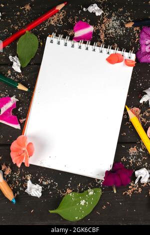 Papier-Notizbuch mit leeren Seiten, zerknitterten Papierkugeln und Buntstiften auf Holzhintergrund, kreatives Schreibkonzept. Ein minimalistischer Arbeitsplatz für einen Stockfoto