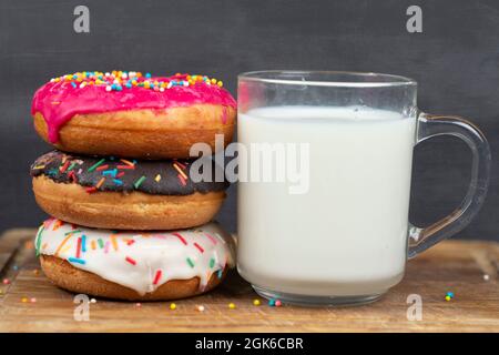 Schönes, süßes Essen. Stapel von glasierten bunten verschiedenen Donuts mit einer Tasse Milch auf einem grauen Hintergrund. Stockfoto