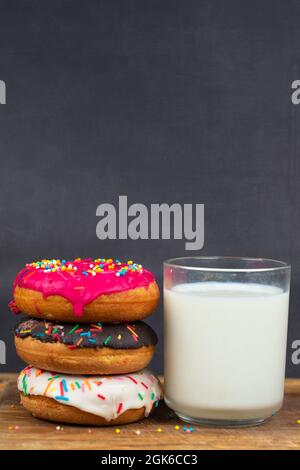 Schönes, süßes Essen. Stapel von glasierten bunten verschiedenen Donuts mit einer Tasse Milch auf einem grauen Hintergrund. Stockfoto