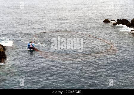 Madeira, Portugal - Februar 2016: Fischer auf einem kleinen Ruderboot, das in einem schweren Fischernetz schleppt Stockfoto